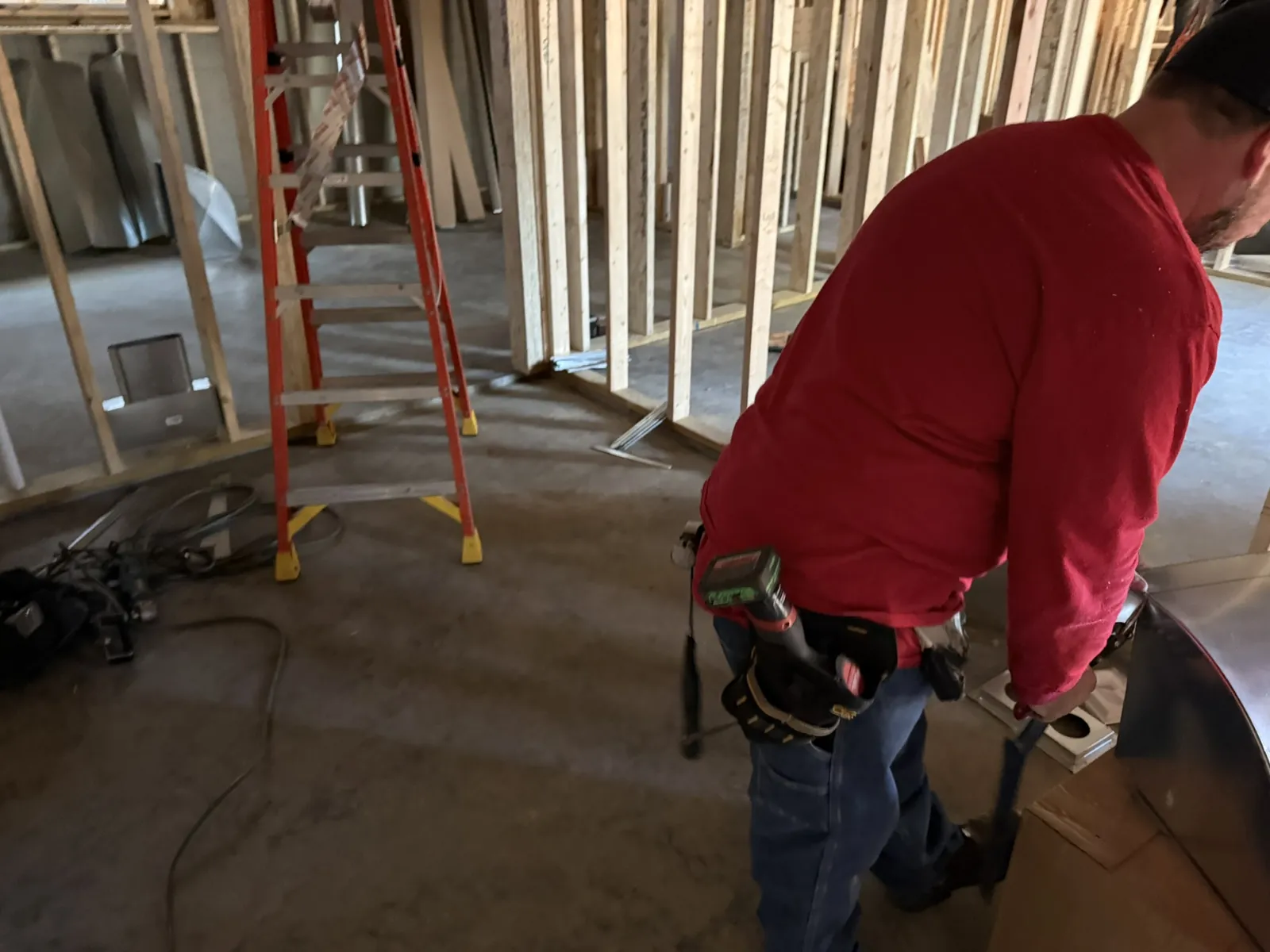 Technician shaping a sheet metal duct fitting on site during a new construction HVAC rough-in