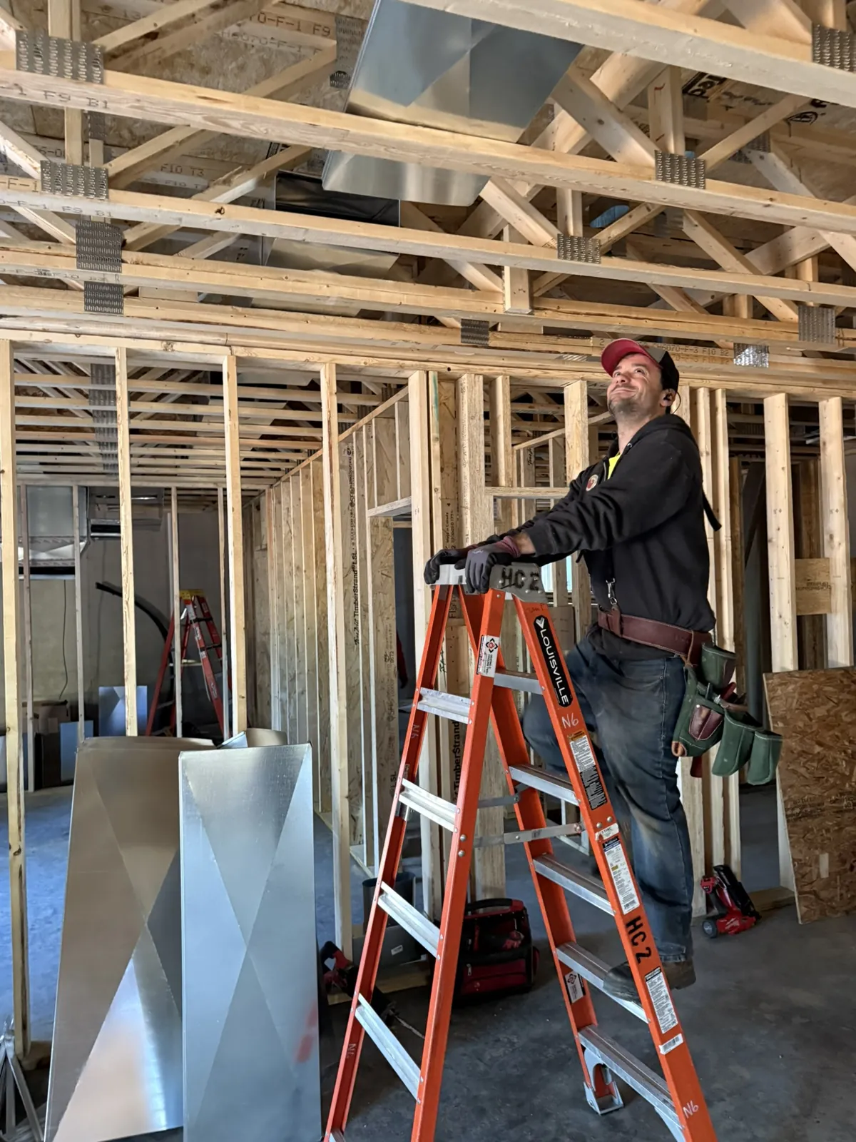 Technician on a ladder securing ductwork to open ceiling framing