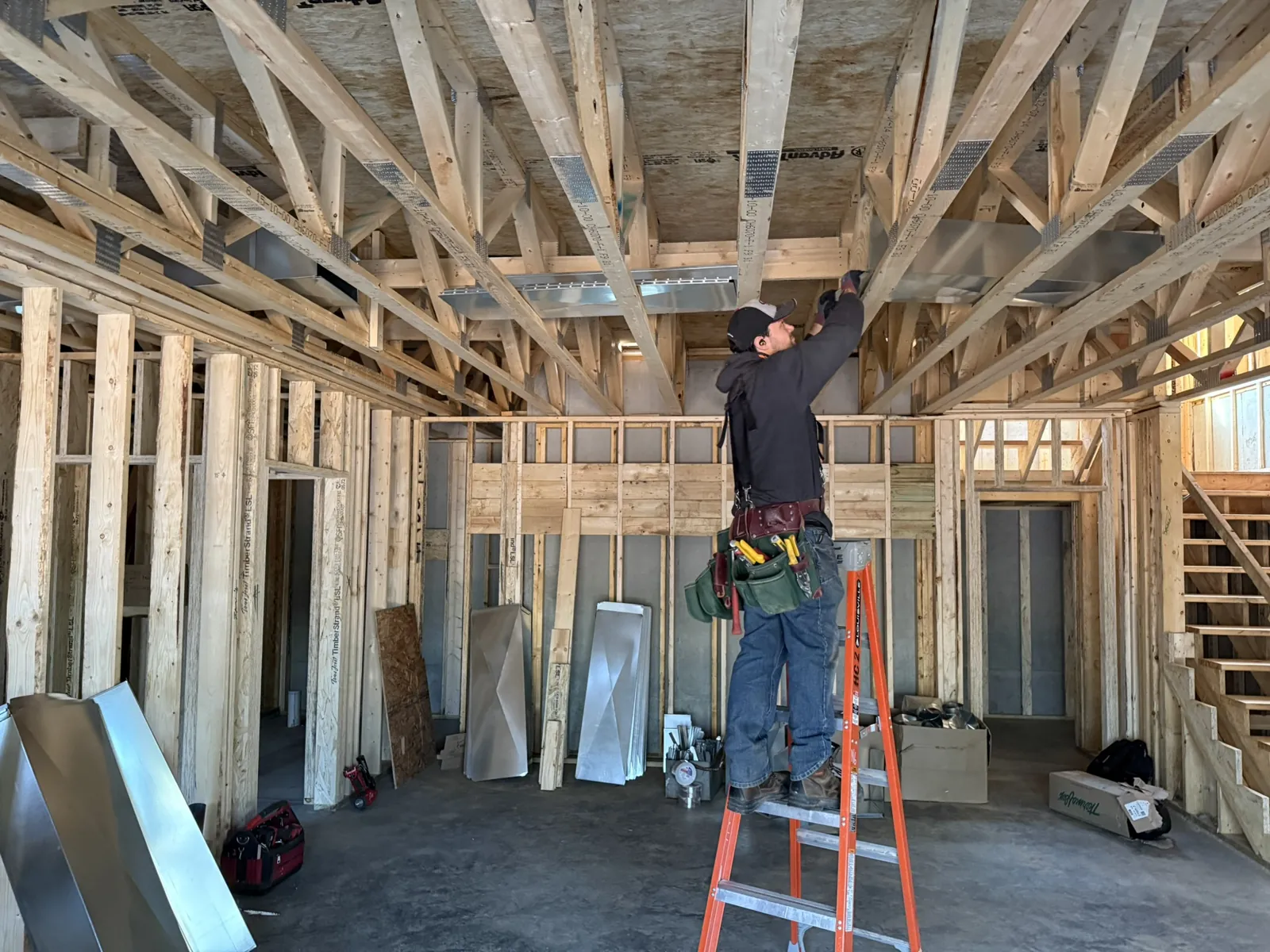 Wide view of a technician hanging ductwork in the ceiling trusses of an open-framed building