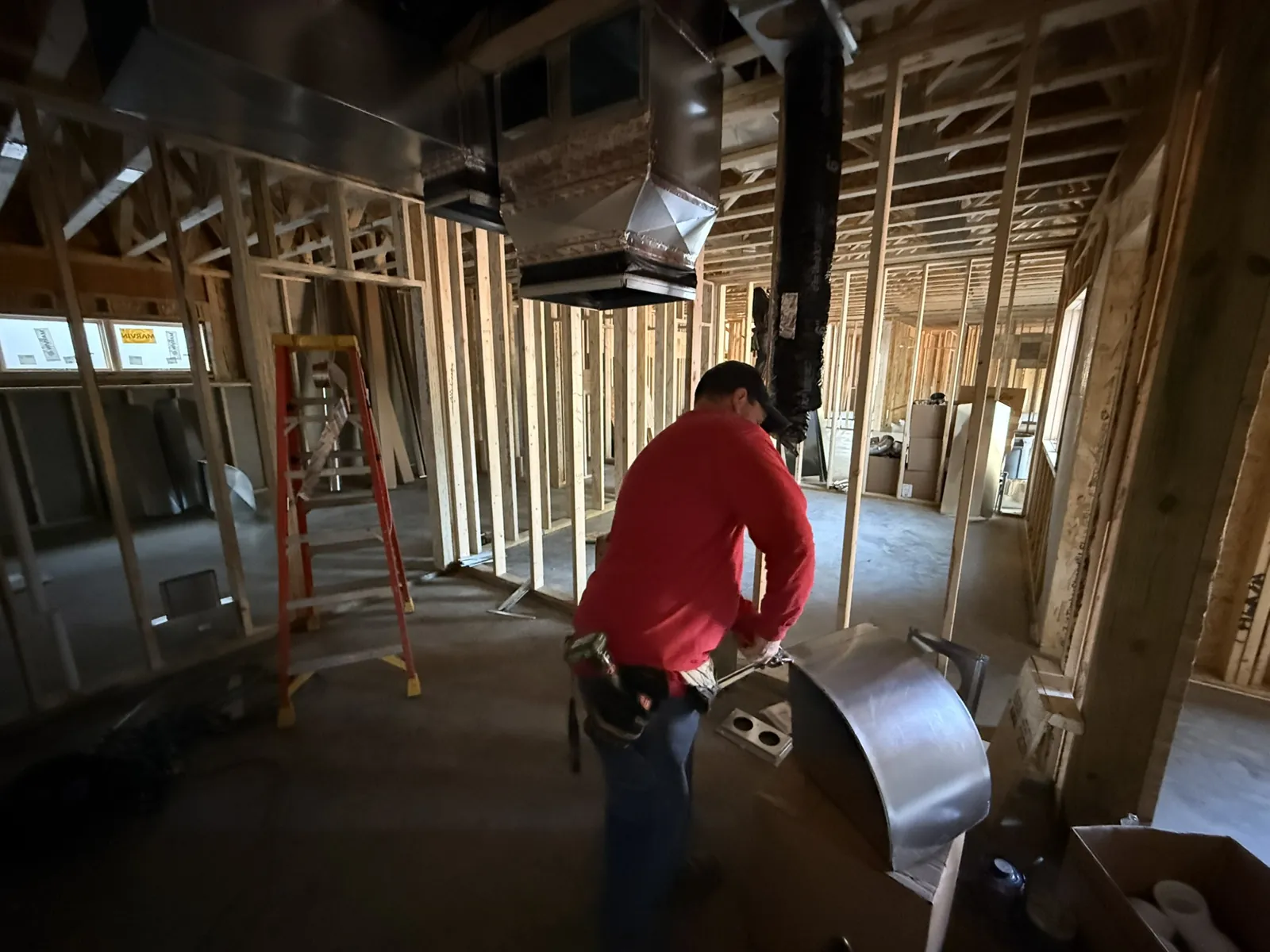 Technician working on round ductwork beneath a newly hung supply trunk in a framed building